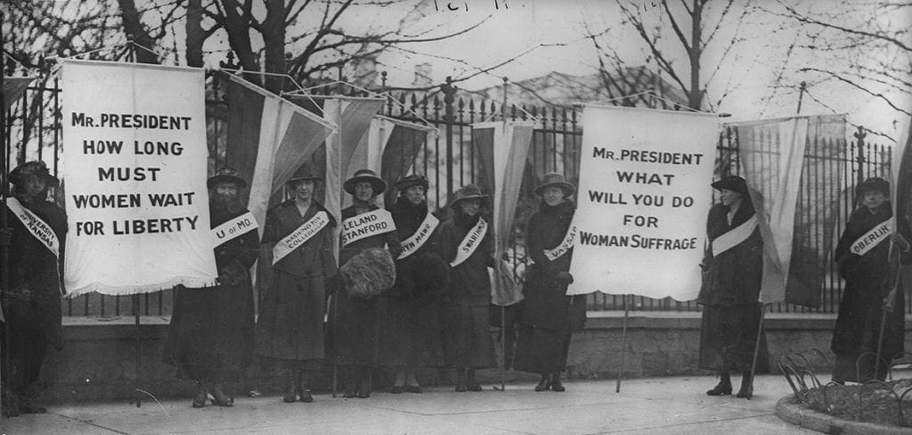 Women picket outside the White House with signs reading "Mr. President How Long Must Women Wait for Liberty" and "Mr. President what will you do for woman suffrage" 