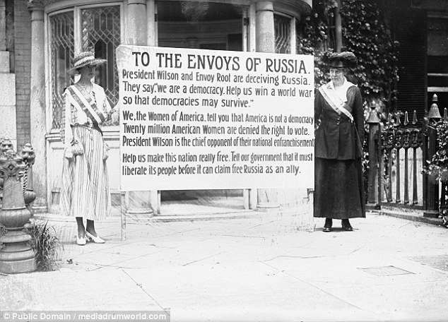 Wome suffragists hold a sign telling Russian envoys that America is not a democracy when twenty million American Women are denied the vote. This is to call the hypocrisy of a nation fighting for democracy abroad