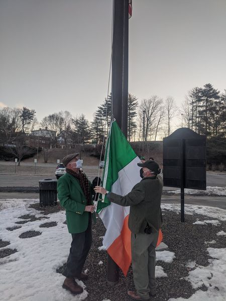 Two men work together to raise the Irish flag in Augusta Maine