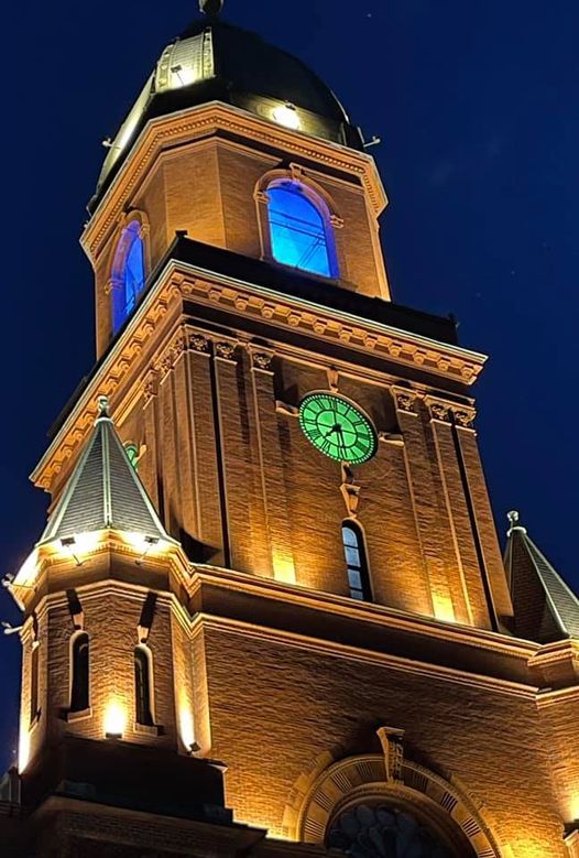 The clock tower of Lewiston Maine's city hall lit up at night with the clock face glowing green.