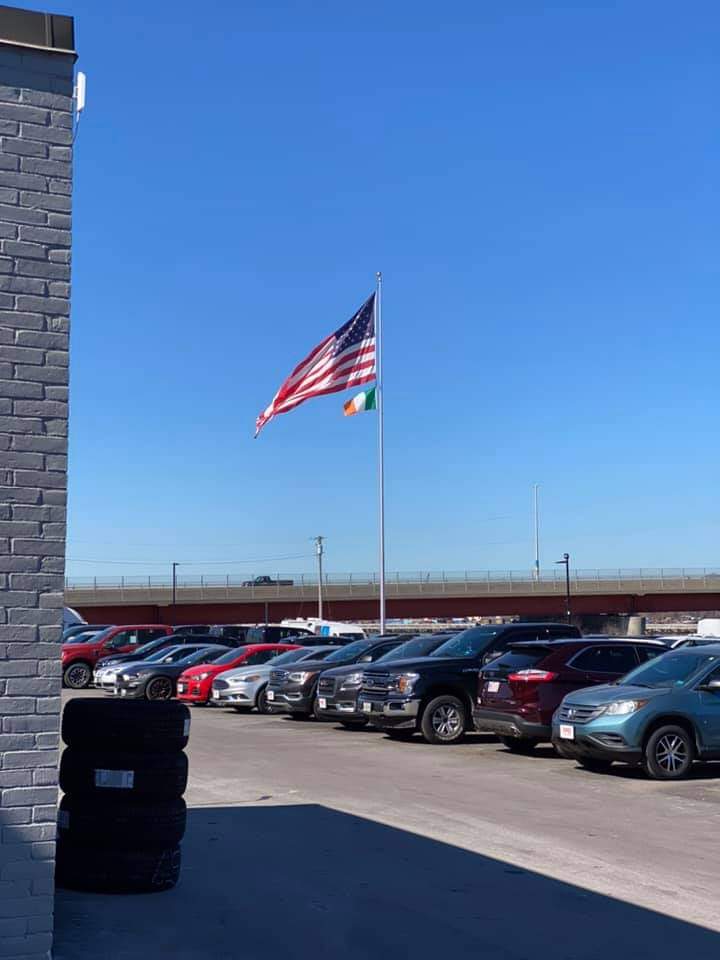 A large American flag flies over a smaller Irish flag over a row of vehicles at Yankee Ford