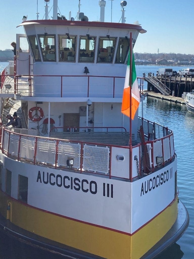 The Irish flag flying on the bow of Casco Bay lines ship, the name Aucocisco three written on the front of the boat. 